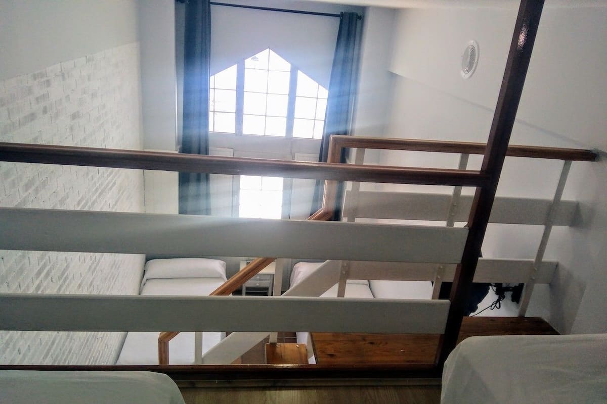 Een studentenkamer met stapelbedden, een raam met gordijnen en een houten vloer.