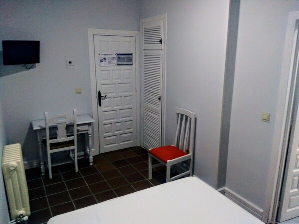 A small, compact room with a bed, a chair with a red cushion, a desk, and a radiator. - Hotel Montesol Arttyco (Monachil)