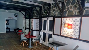 Un intérieur moderne avec un mélange de chaises rouges et grises, un sol carrelé et un mur en pierre orné d’un motif géométrique.
