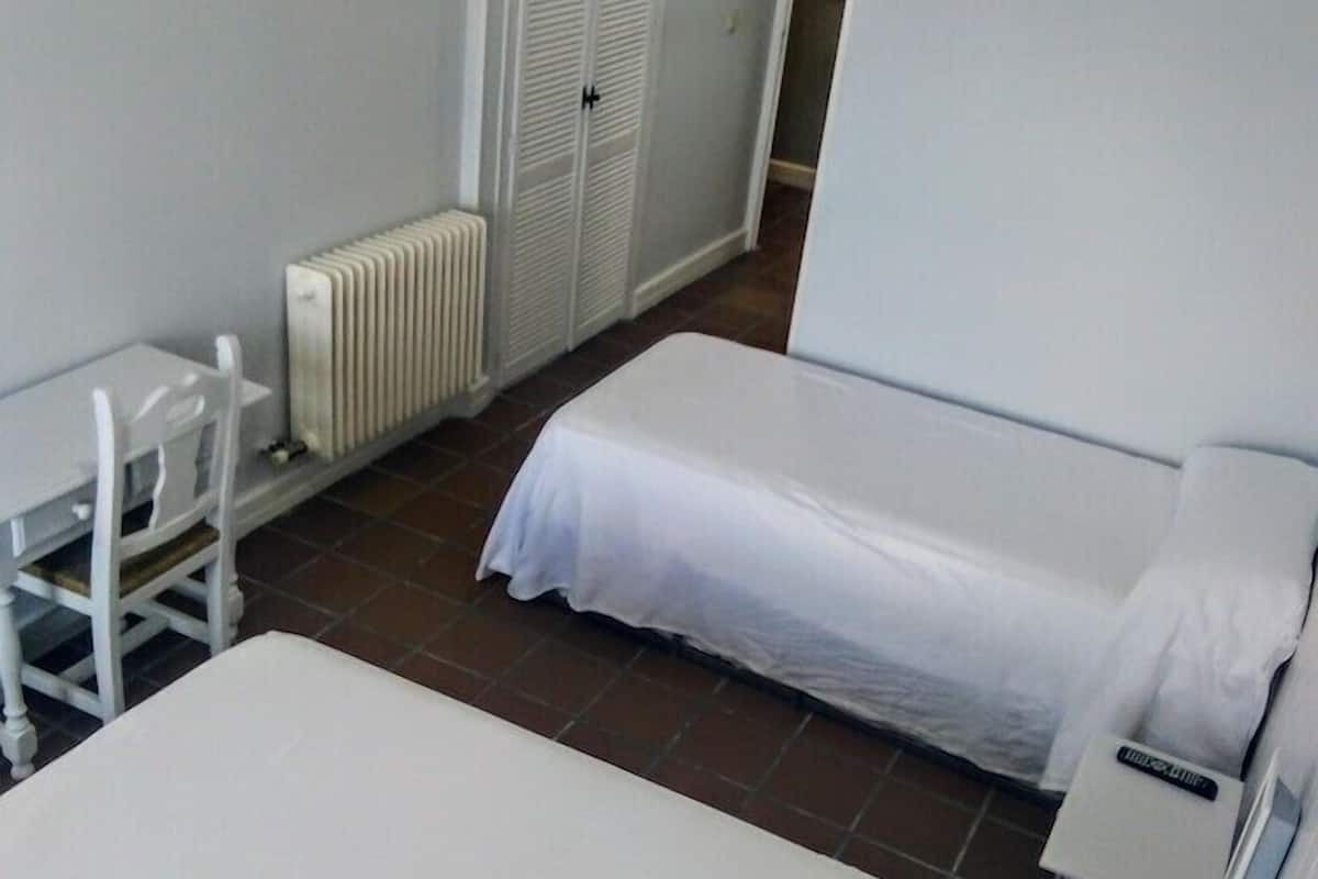 Een kleine, schone kamer met twee bedden, een stoel, een radiator en een kast.