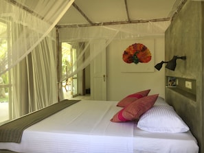 Une chambre avec un lit, une moustiquaire, une décoration murale représentant un oiseau et une lampe.