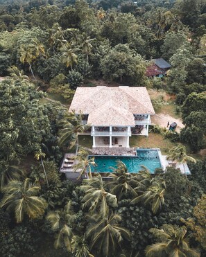 Une maison à deux étages, dotée d’un toit en tuiles et entourée d’une végétation tropicale luxuriante.