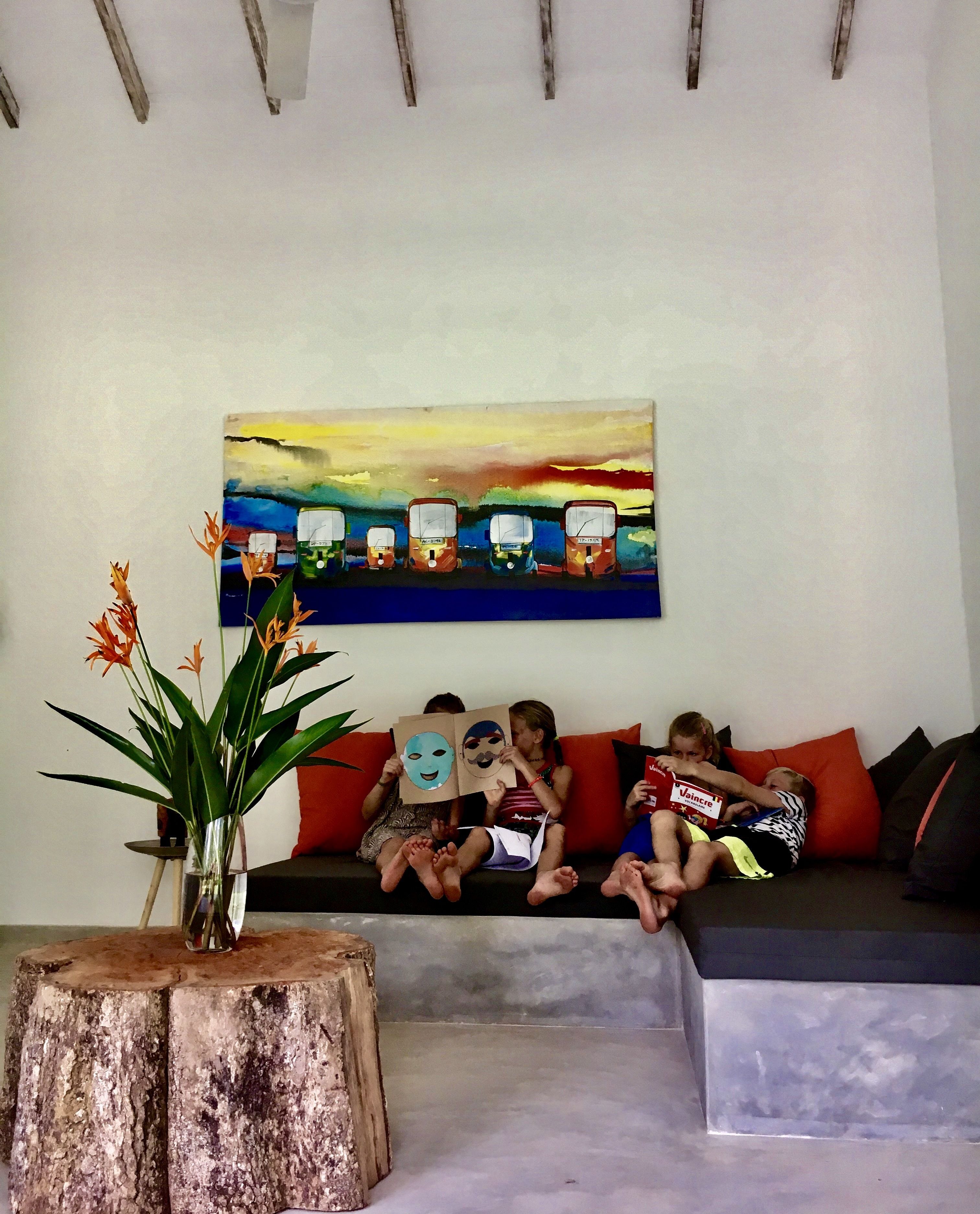 A living room with a sofa, a painting on the wall, and a plant on a wooden stool.