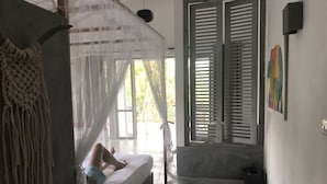 A room with a bed under a mosquito net, a large window with shutters, and a macrame wall hanging. - Good Vibes Villas Retreat And Restaurant (Unawatuna)