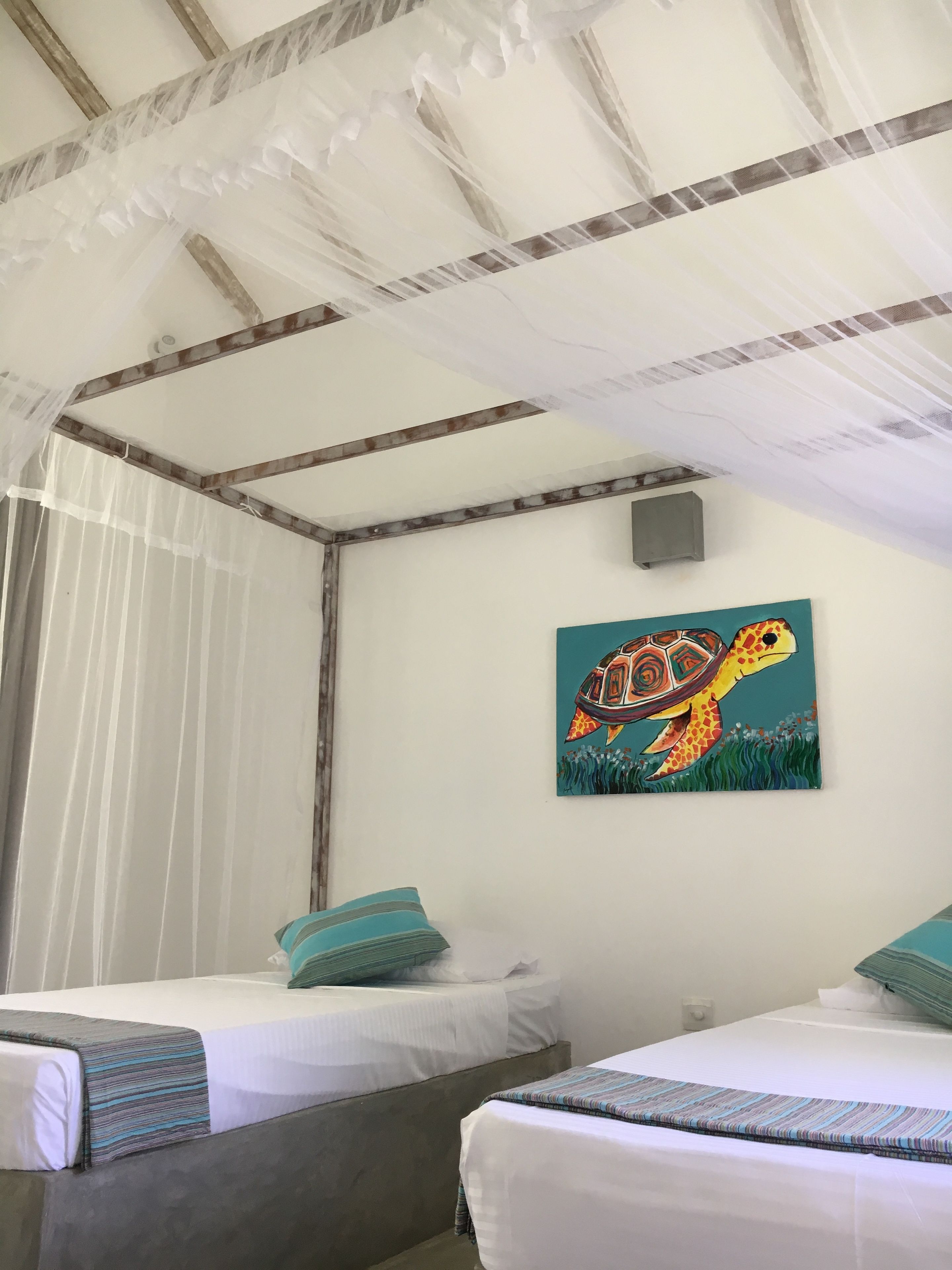 Une chambre avec deux lits, une moustiquaire et un tableau représentant une tortue accroché au mur.