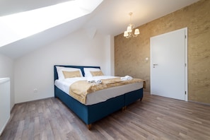 Ein Schlafzimmer mit einem Oberlicht, einem Bett mit blauer Kopfteil, Holzboden und einer weißen Tür.