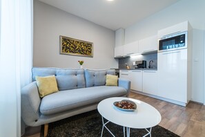 A modern living room with a grey sofa, a white coffee table, and a kitchen area with white cabinets and appliances. - MyApartment in the city center (Ceske Budejovice)