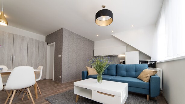Una sala de estar moderna con un sofá azul, una mesa de centro blanca y un comedor con sillas blancas.