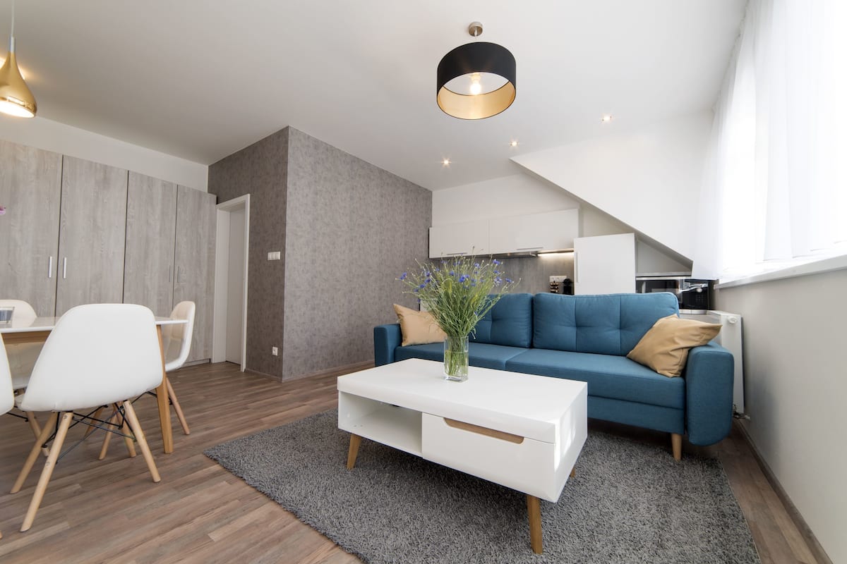 A modern living room with a blue sofa, white coffee table, and a dining area with white chairs.