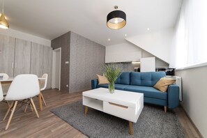 Ein modernes Wohnzimmer mit einem blauen Sofa, einem weißen Couchtisch und einem Essbereich mit weißen Stühlen.