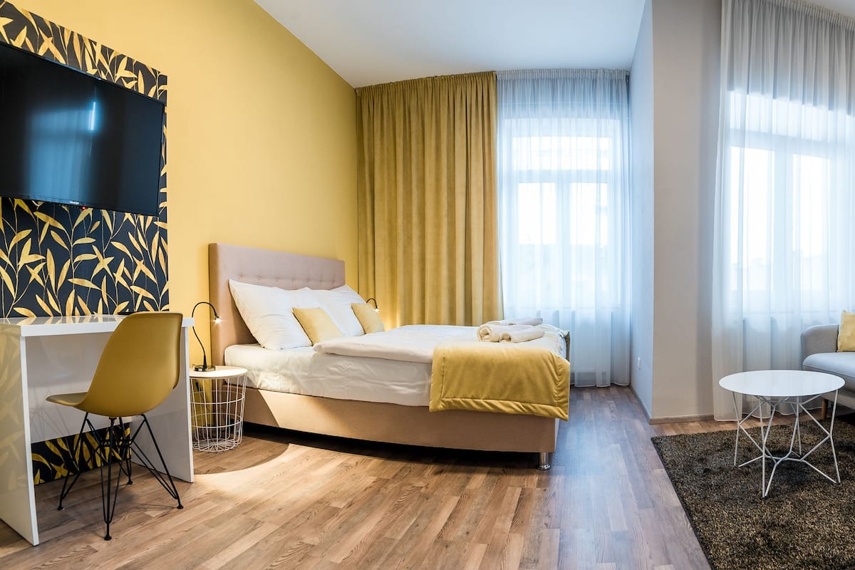 A modern hotel room with a bed, a sofa, a desk, and a TV.