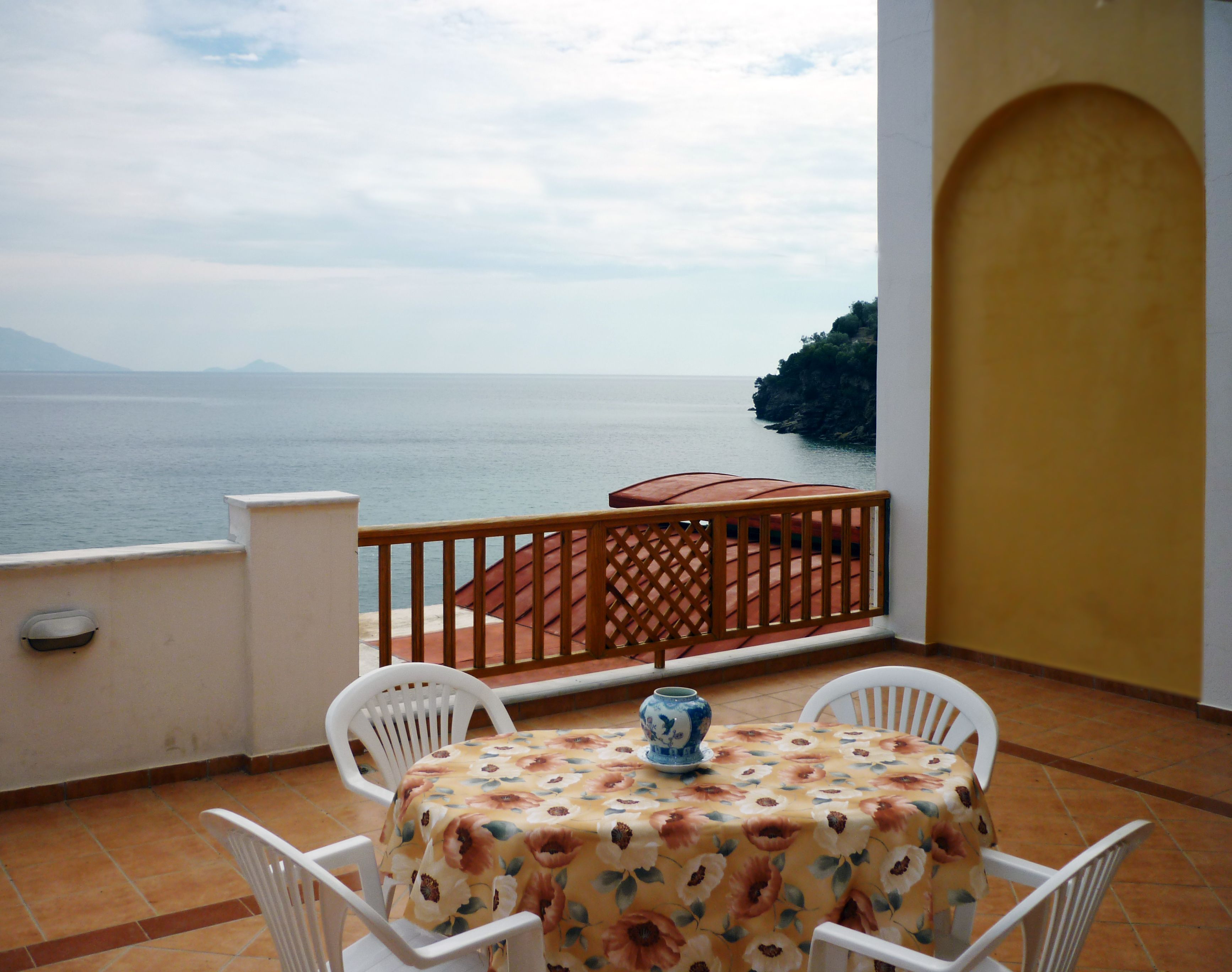 A balcony with a table and chairs, overlooking a body of water and a distant landmass.
