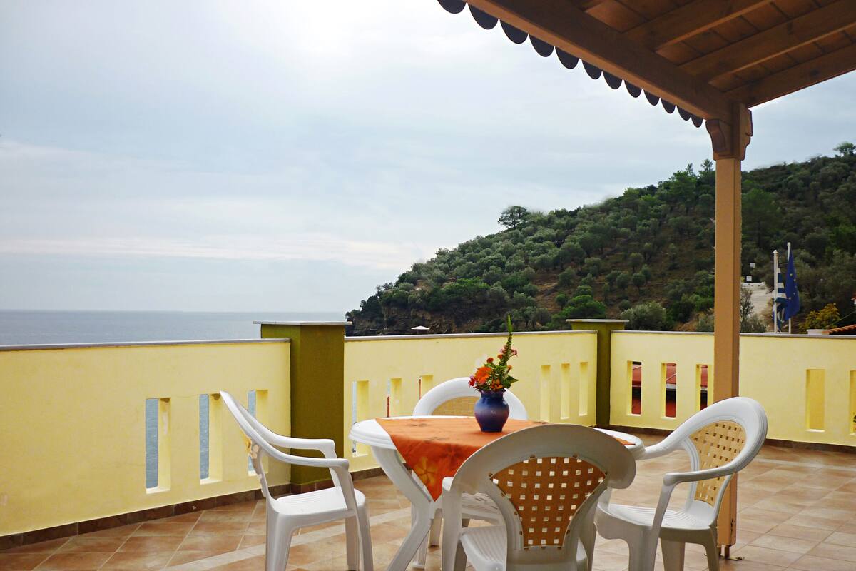 A terrace with a table and chairs, overlooking a coastal landscape.