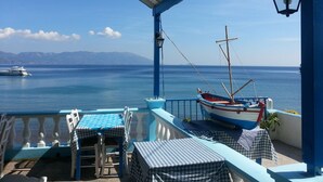 Eine Terrasse mit Blick auf das Meer, ein Boot und ein Tisch mit Stühlen.