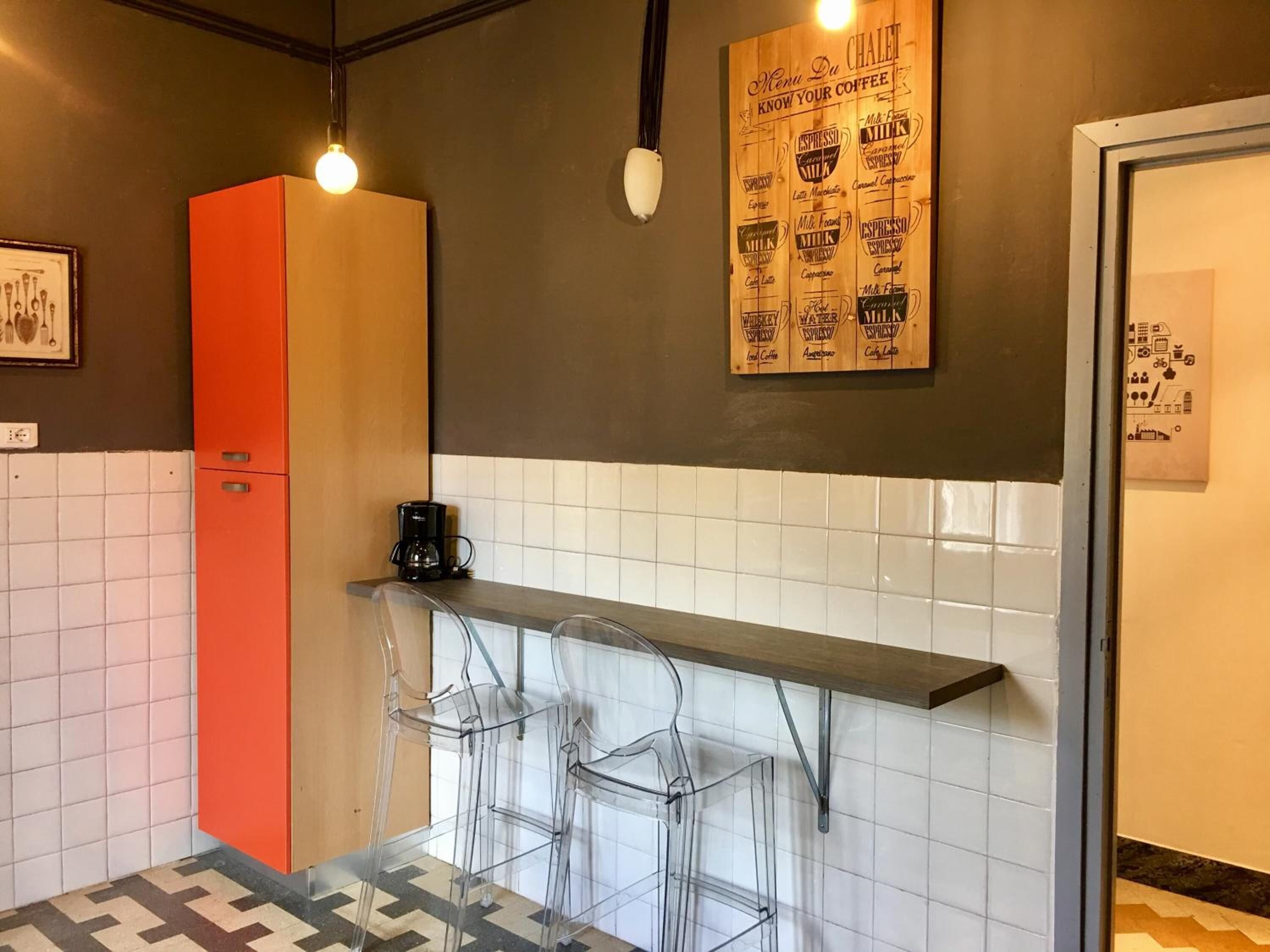Eine kleine Küche mit einem roten Schrank, einer Kaffeemaschine und einer Bar mit transparenten Stühlen.