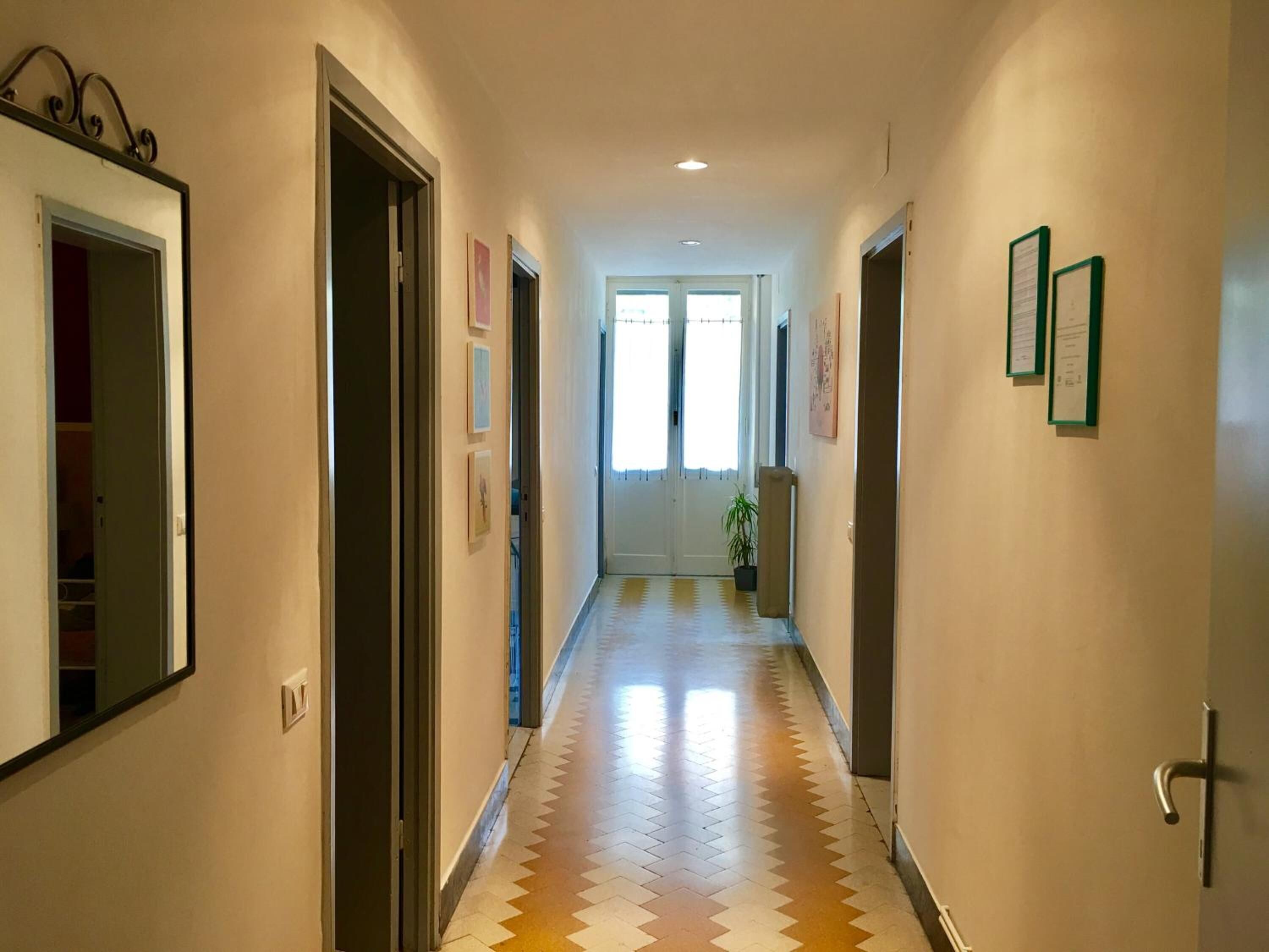 Un couloir avec un sol à motifs à carreaux, des portes de part et d’autre, et des tableaux encadrés accrochés aux murs.