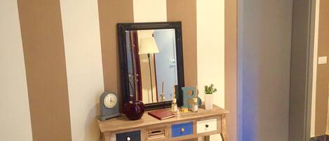 Una consola de madera con un espejo, un reloj, una lámpara y algunos objetos decorativos.