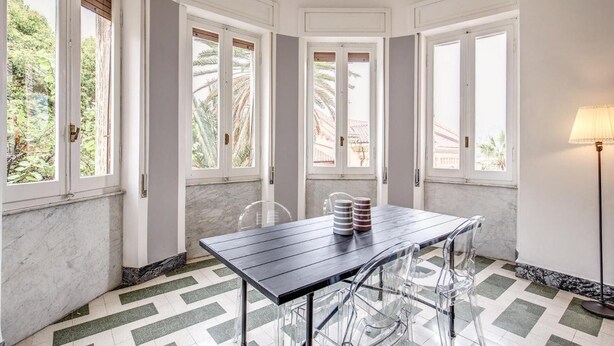 Comedor con una mesa de madera oscura, sillas transparentes y vistas a palmeras a través de las ventanas.