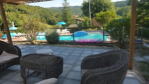 Een terras met rieten meubels, een zwembad met opblaasbare luchtbedden en uitzicht op een bebost dal.