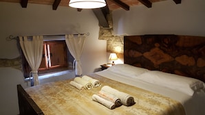 Een slaapkamer met een houten hoofdbord, een bed met witte lakens, een nachtkastje met een lamp en een raam met gordijnen.