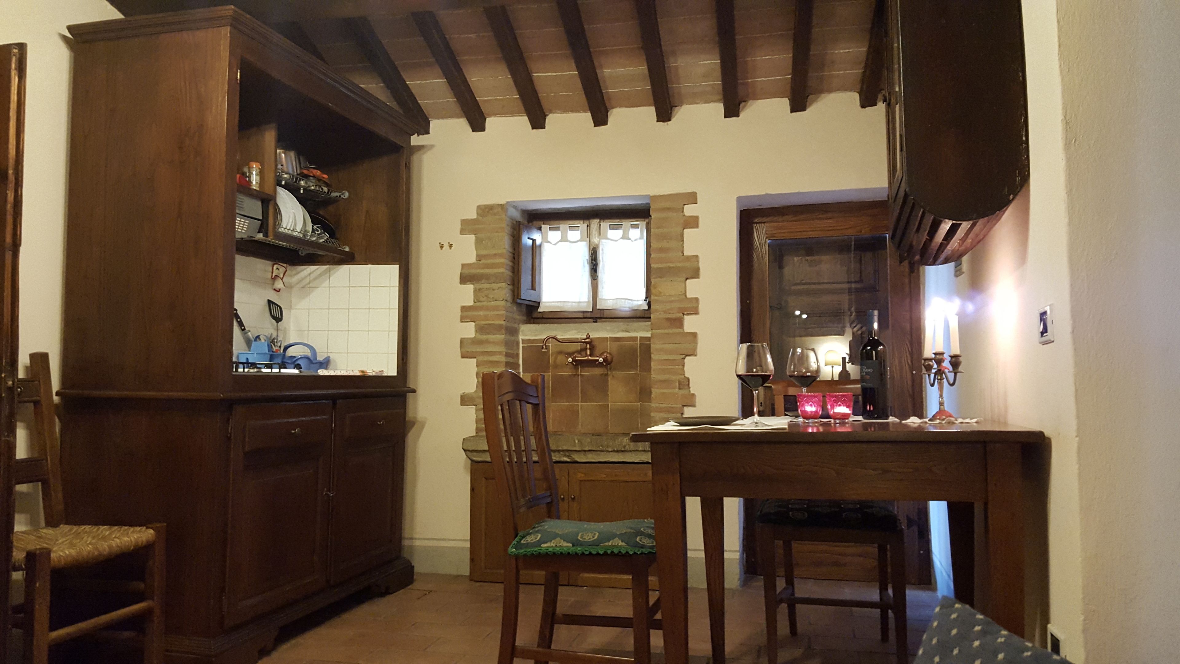 A kitchen with wooden cabinets, a tiled backsplash, a window with curtains, and a dining table with chairs.