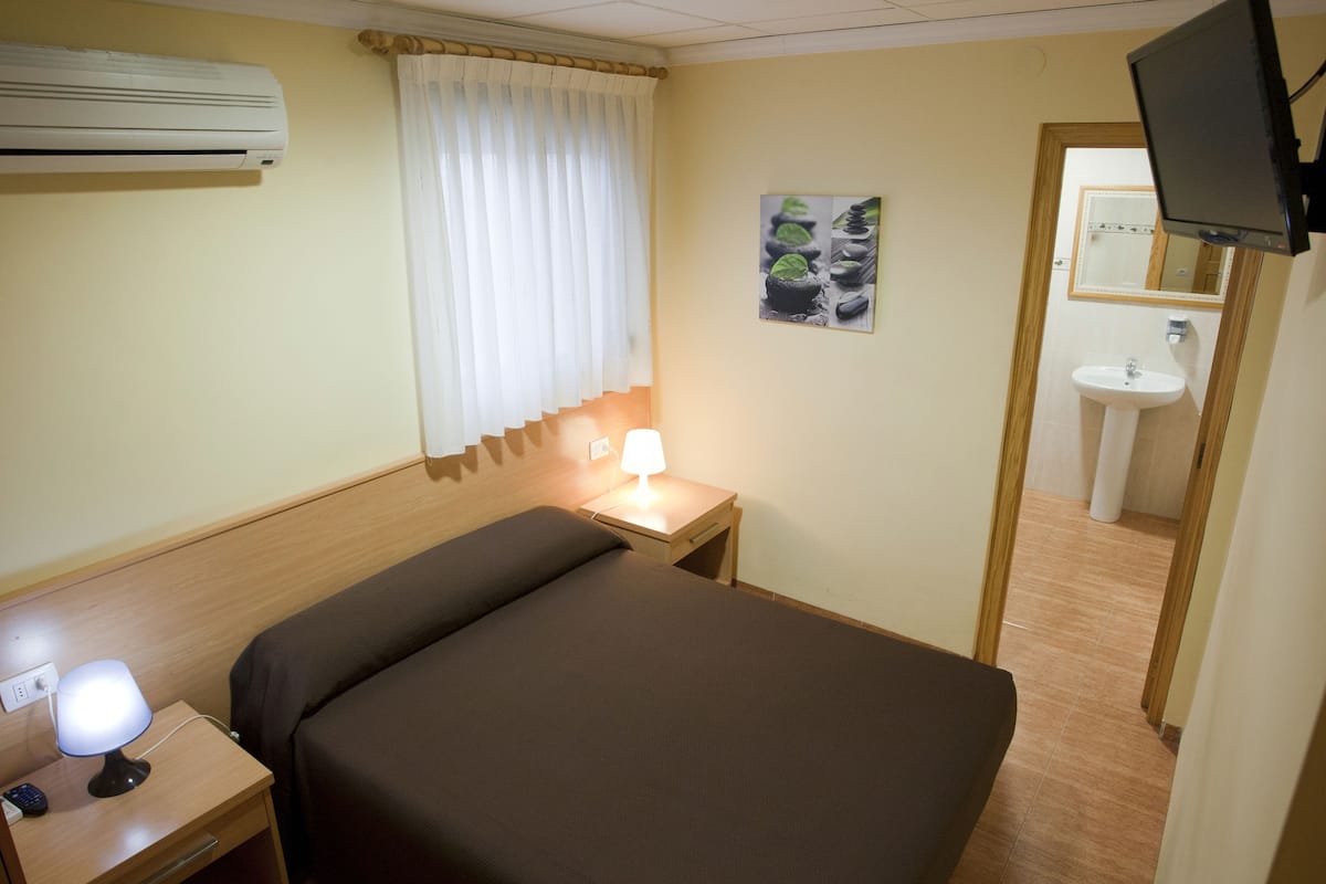 Ein Hotelzimmer mit Bett, Nachttischlampe, Klimaanlage und Blick ins Badezimmer durch eine offene Tür.