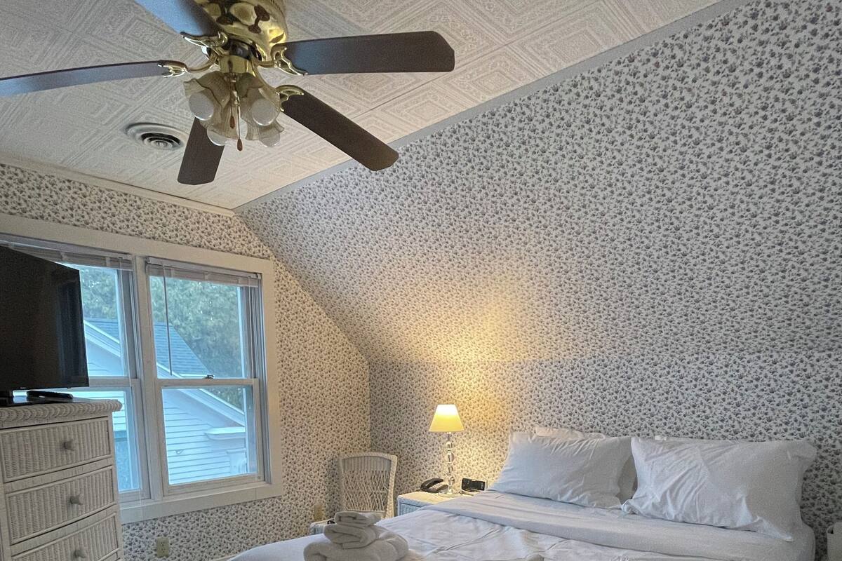 A bedroom with a bed, a dresser, a nightstand, a lamp, and a ceiling fan.