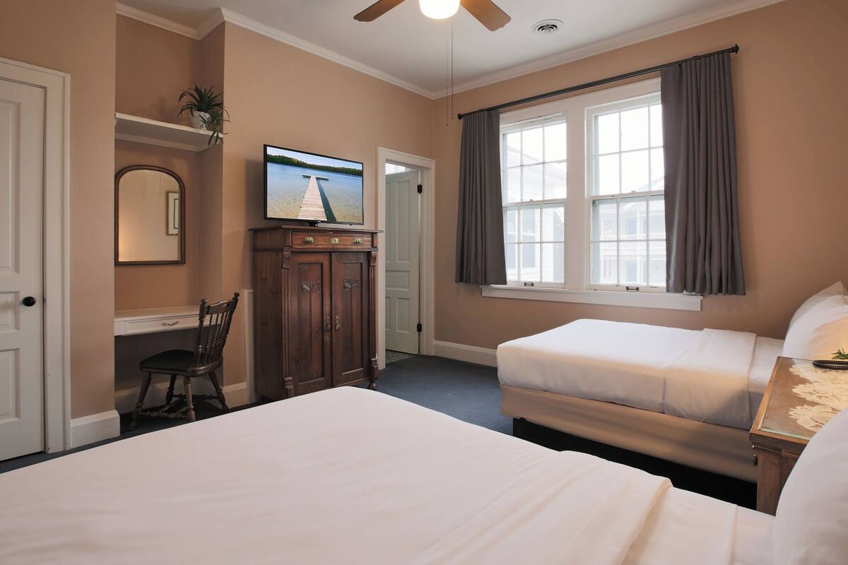 A hotel room with two beds, a TV, a desk with a chair, and a window with curtains.