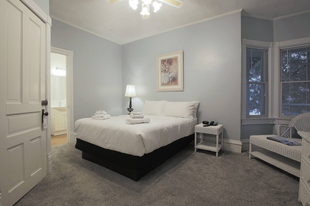 A bedroom with a bed, bedside table, lamp, and a window with blinds.