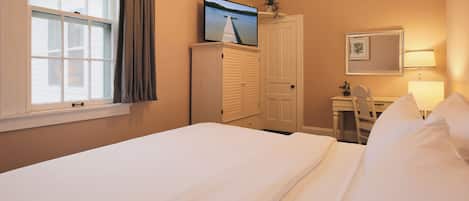 A hotel room with a large bed, a desk with a chair, a wardrobe, a television on a stand, and a window with curtains.