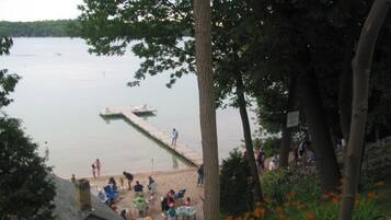 A lakeside scene with a dock extending into the water, surrounded by trees and a small building with people gathered around.