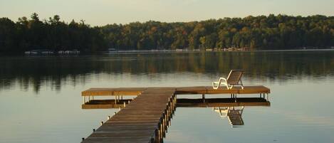 A wooden pier extending into calm water with a single white lounge chair at the end.