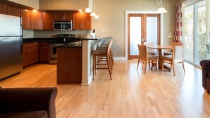 A modern kitchen with wooden cabinets, a stainless steel refrigerator, and a dining area with a table and chairs. - Siebkens Resort (Elkhart Lake)