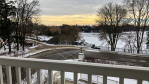 A view from a balcony overlooking a snow-covered landscape with a road, trees, and a distant building. - Siebkens Resort (Elkhart Lake)