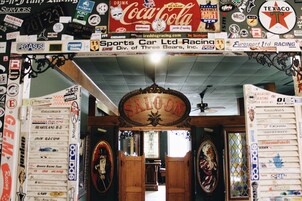 Quarto com porta de madeira com a inscrição 'SALOON' e diversos adesivos de corridas e automóveis nas paredes.