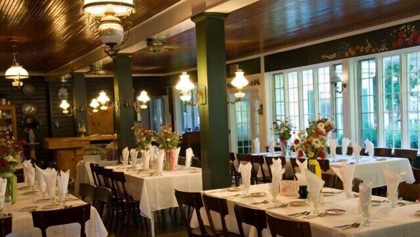 A restaurant with multiple tables set for dining, featuring white tablecloths and floral centerpieces. - Siebkens Resort (Elkhart Lake)