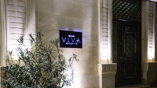 Ein Blumentopf mit Pflanze vor einem Gebäude, dessen Schild 'VIVA' zeigt.