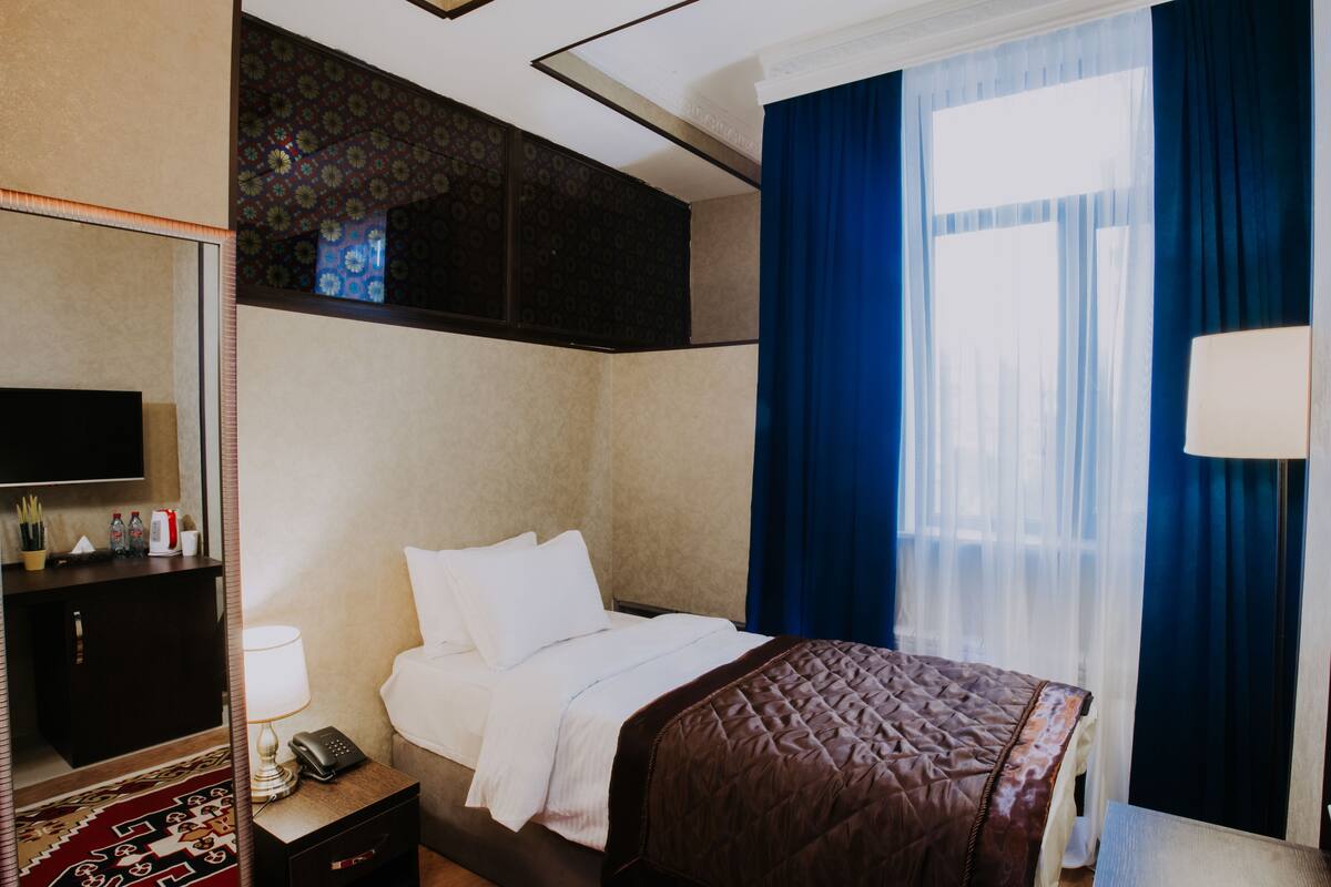 Une chambre d’hôtel avec un lit, une table de chevet avec une lampe, un téléphone et un téléviseur fixé au mur.