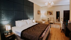 Ein Hotelzimmer mit einem großen Bett, einem dunklen Kopfteil, einer Kandelaber und einem Schreibtisch mit Stuhl sowie einem Spiegel.