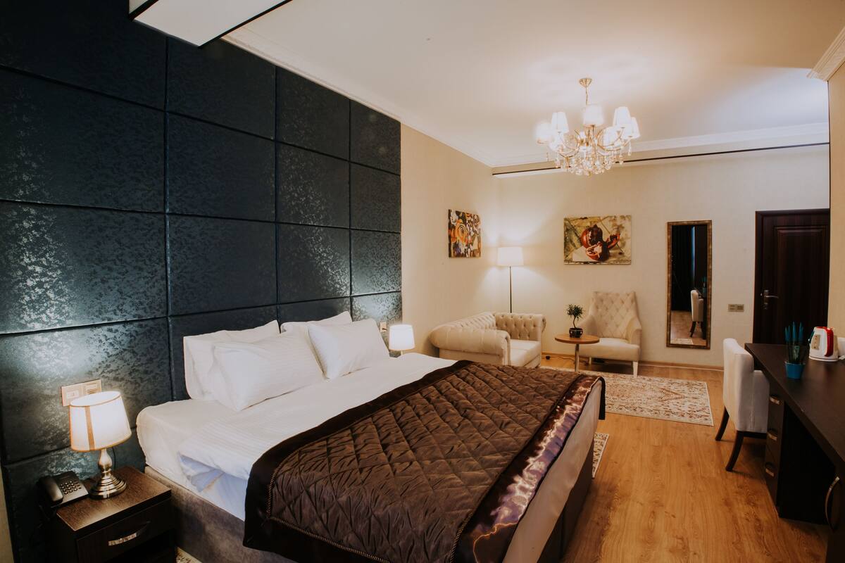 Une chambre d’hôtel avec un grand lit, une tête de lit sombre, un lustre, un bureau avec une chaise et un miroir.