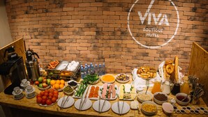 Ein reichhaltiges Buffet mit verschiedenen Speisen und Getränken, eine Kaffeemaschine sowie eine Backsteinwand mit dem Logo "Viva Boutique Hotel".