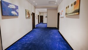 Ein Flur mit blauem Teppich, weißen Wänden und Kunstwerken an den Wänden.
