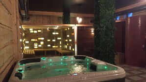 Un jacuzzi con iluminación verde, rodeado de paredes de madera y una zona de estar con mesas y sillas.
