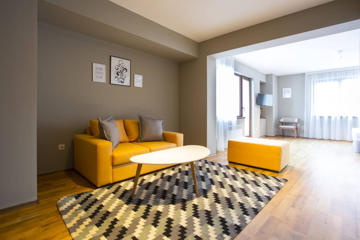 Ein modernes Wohnzimmer mit einem gelben Sofa, einem weißen Couchtisch und einem gemusterten Teppich.