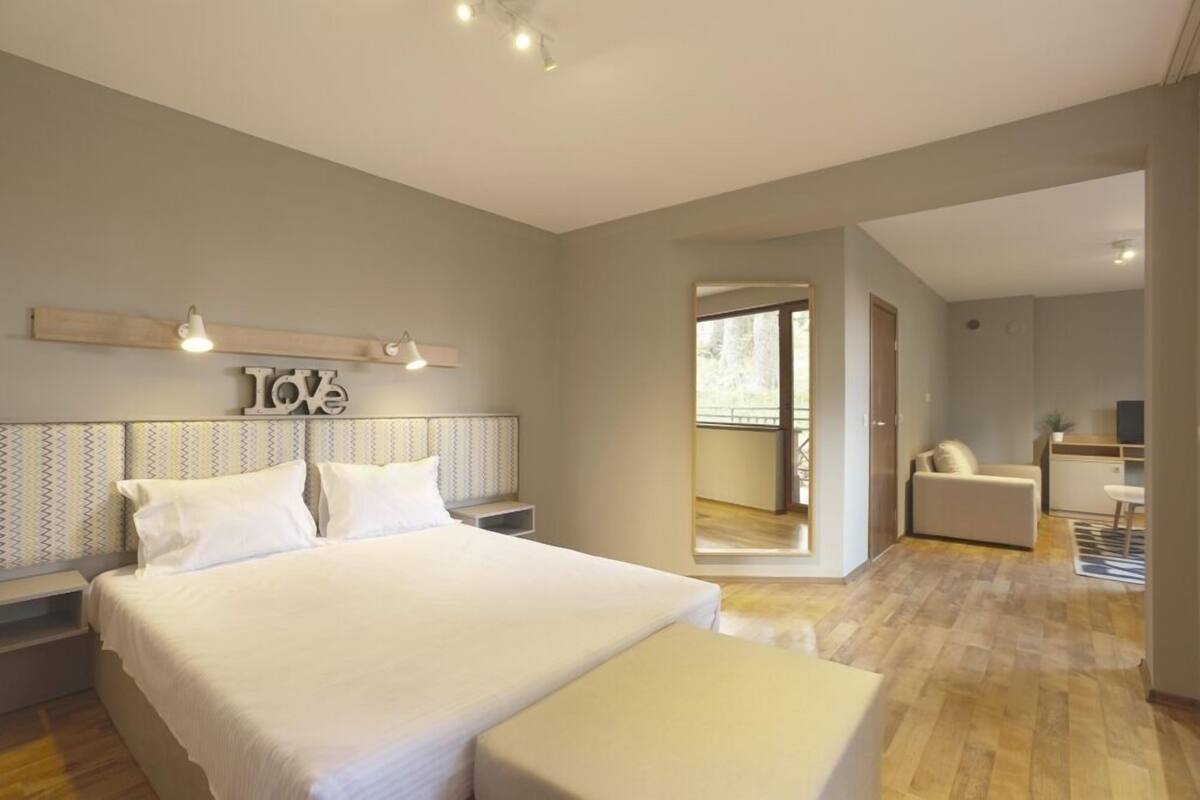 Ein modernes Schlafzimmer mit einem großen Bett, Nachttischen, einem Spiegel und Blick auf einen Balkon.