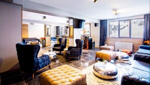 Un amplio salón con un ventanal grande, una chimenea y diversas opciones de asientos, incluyendo un otomano capitonado y sillones.