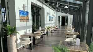 Een modern buitenontbijtgedeelte met tafels en stoelen, potplanten en uitzicht op de straat.
