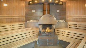 Een sauna met houten banken, een haard in het midden en een stenen muur.