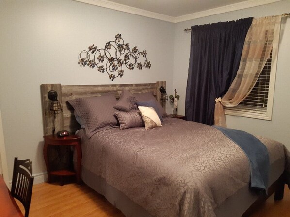 A bedroom with a bed, a nightstand, a wall art piece, and a window with curtains.