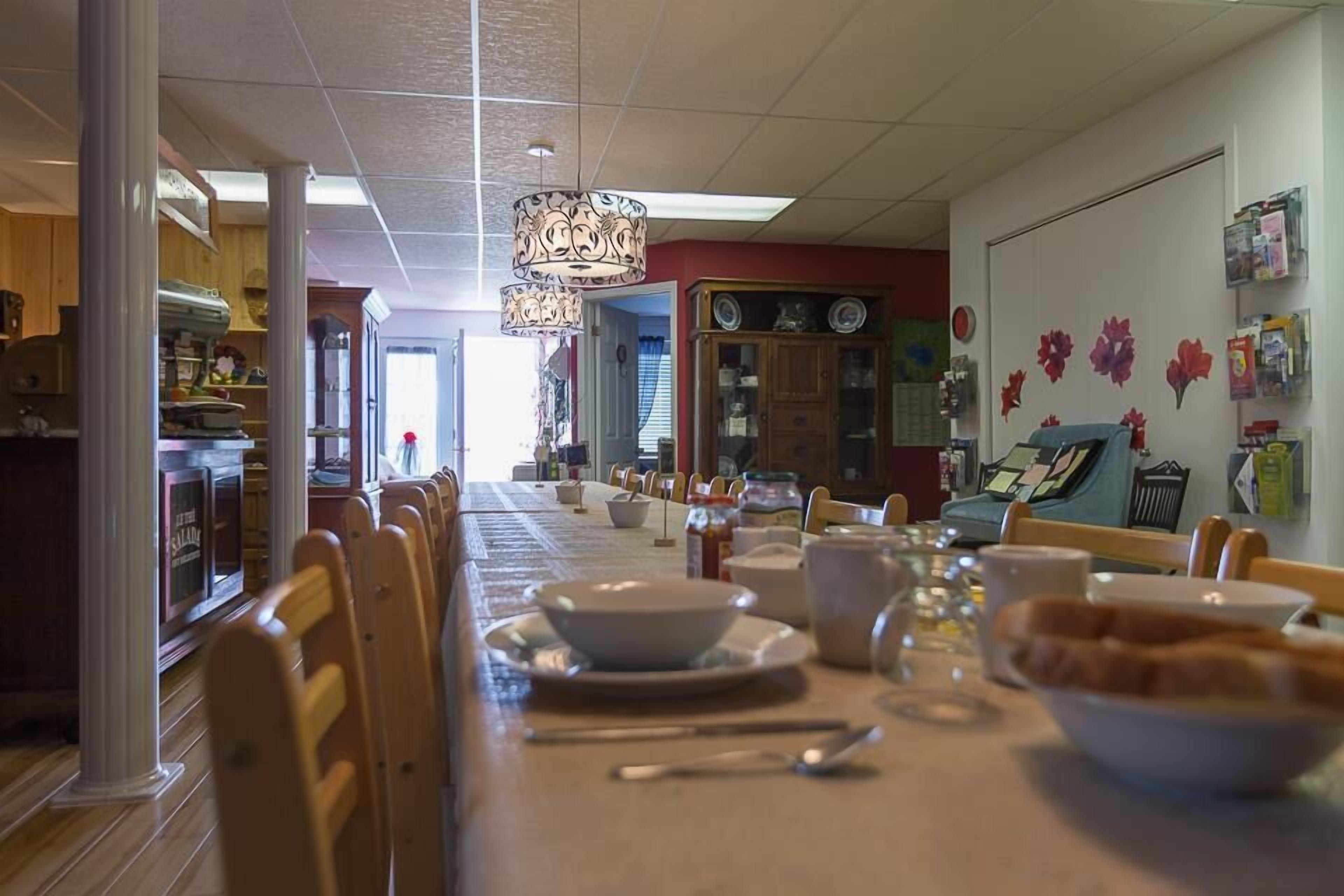 A dining area with a long table set for a meal, chairs, and a cabinet with dishes.